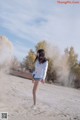 A woman in a white shirt and blue shorts standing in the sand.